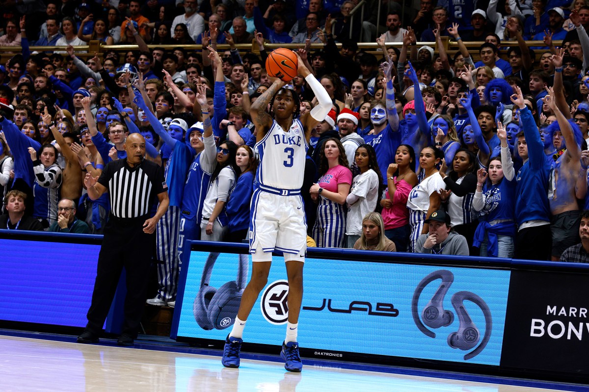 Duke freshman Isaiah Evans with the ball in his hands about to take a three-pointer as the crowd cheers behind him.