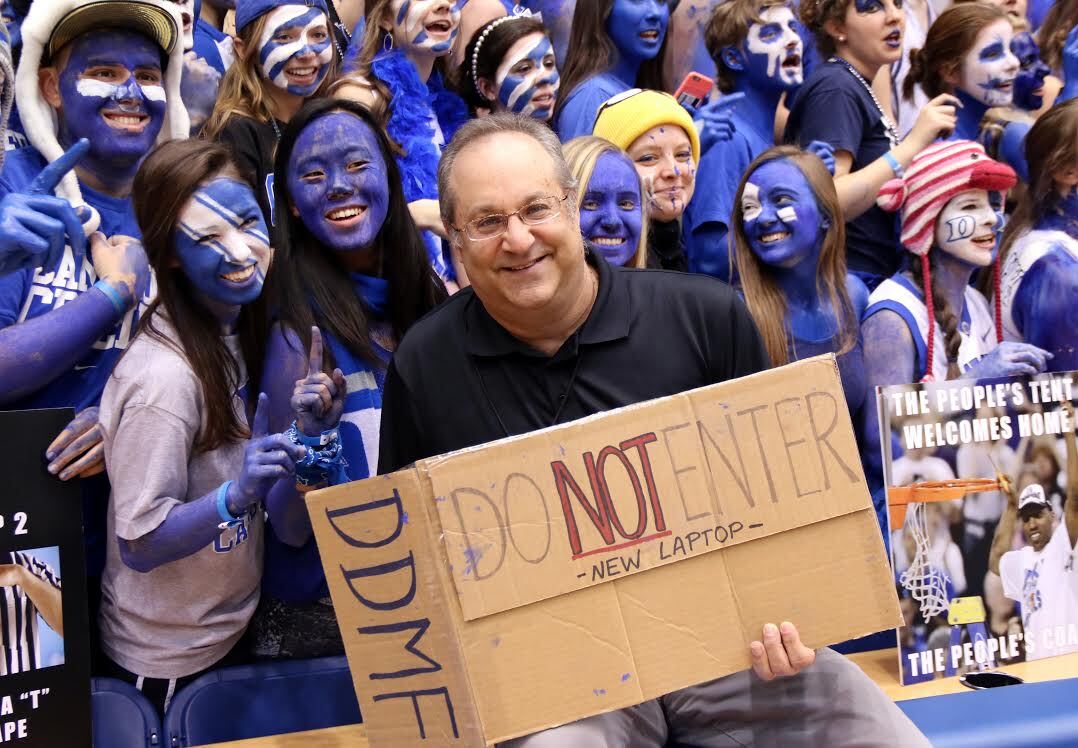 Image of Brett Friedlander posing with "Cameron Crazies" as he holds a carboard sign that reads: "Do Not Enter. New Laptop."
