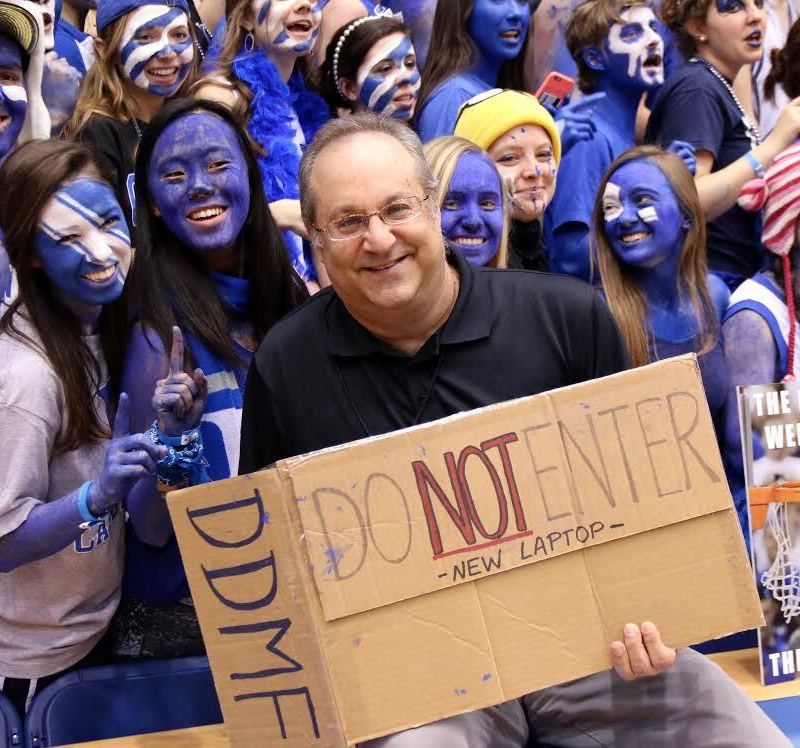 Image of Brett Friedlander posing with "Cameron Crazies" as he holds a carboard sign that reads: "Do Not Enter. New Laptop."